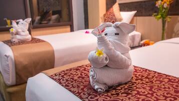 A hotel room with two beds, each with a towel animal sculpture and a flower.