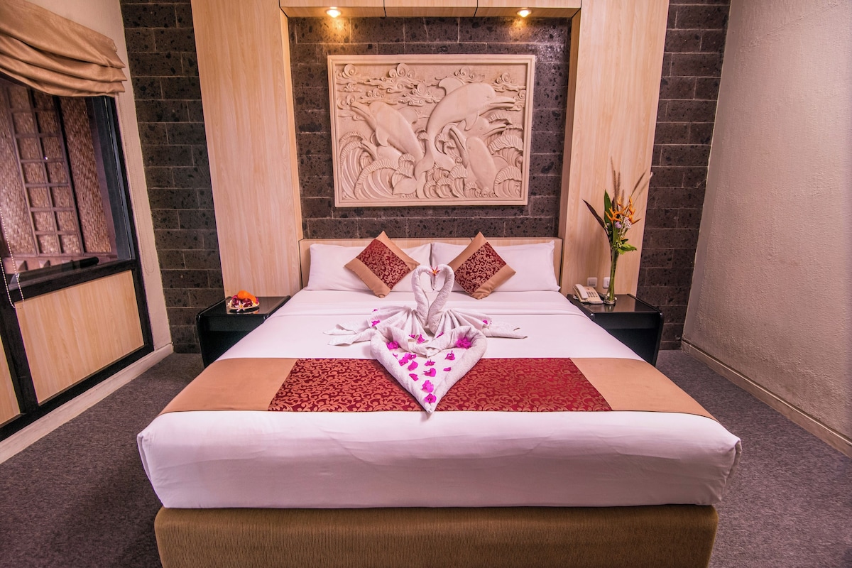 Een hotelkamer met een groot bed, een decoratief wandobject en een nachtkastje met een telefoon en een bloevas.