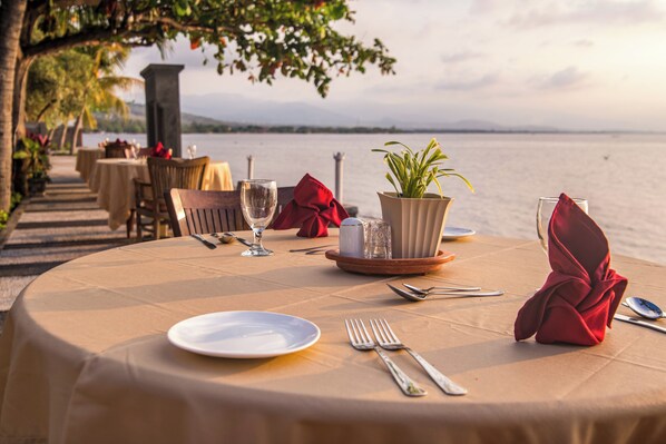 A table set for dining with a view of the sea, a potted plant, and a red napkin.
