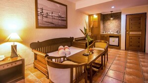 Un coin repas avec une table en bois, des chaises, un canapé, une lampe, un tableau encadré au mur et, au fond, un espace cuisine.