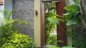 Un bâtiment moderne avec une façade en pierre, une porte en bois et une végétation tropicale luxuriante.
