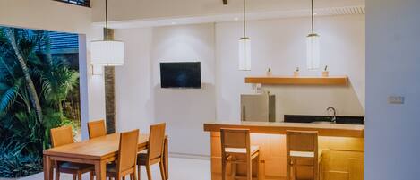 A modern kitchen with wooden cabinetry, a dining area with a wooden table and chairs, and pendant lighting.