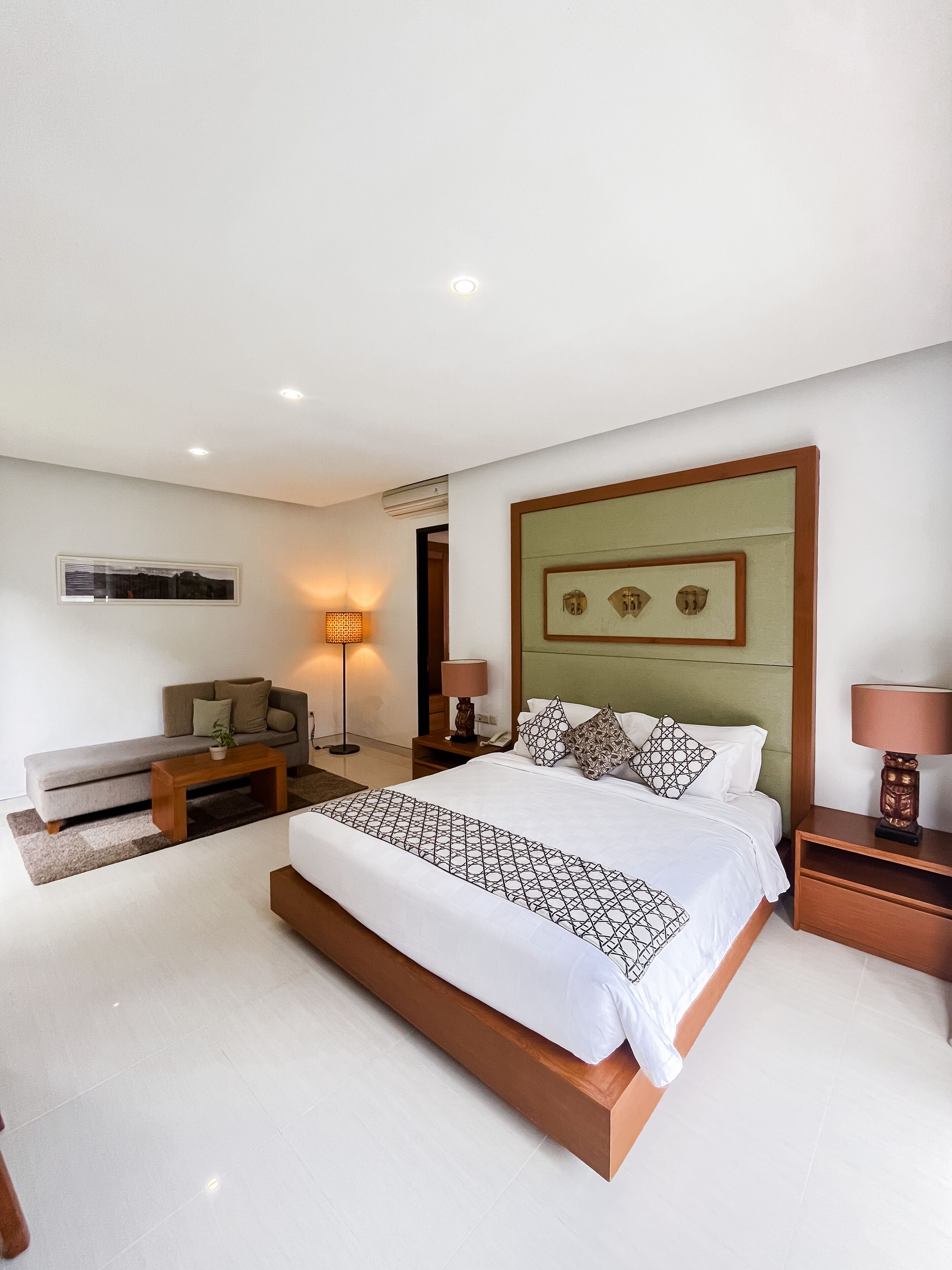 A modern bedroom with a large bed, a sofa, a bedside table, and a lamp.