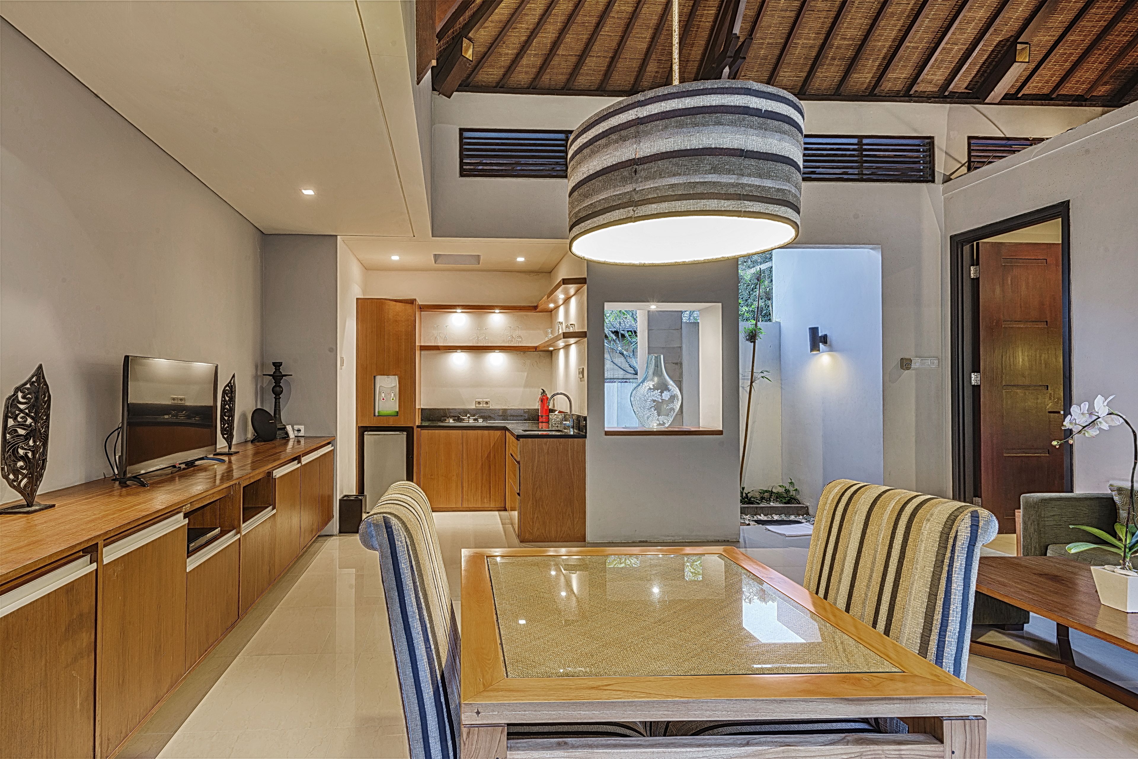 A modern kitchen with wooden cabinets, a dining area with a glass-top table, and a large hanging light fixture.