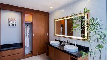 A modern bathroom with two sinks, a large mirror, wooden cabinets, and a potted plant.