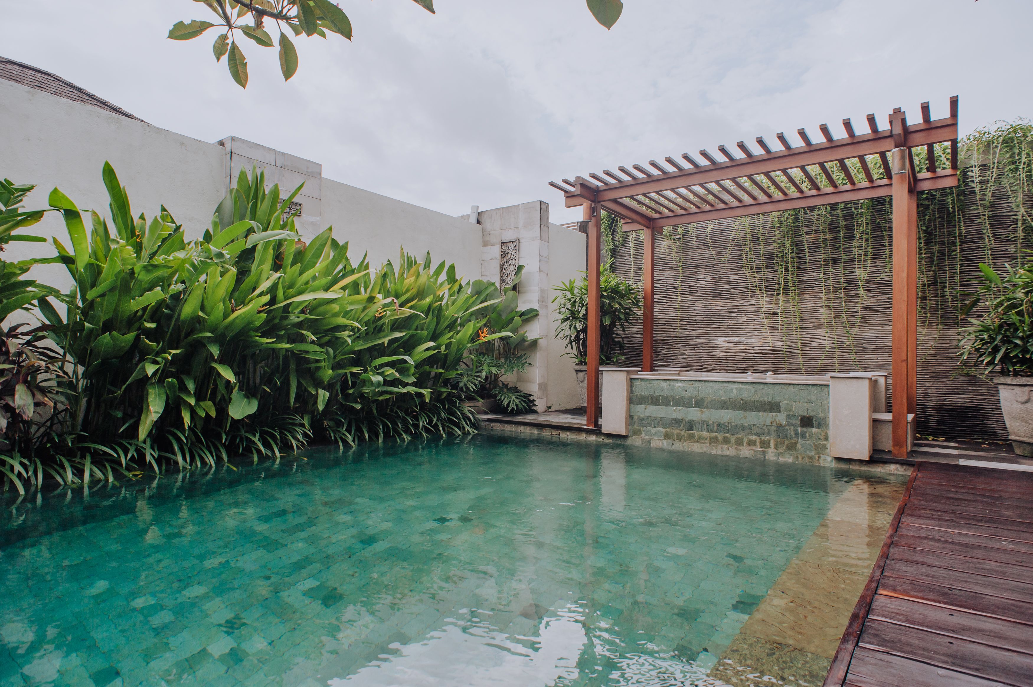A clear swimming pool with a wooden deck and a pergola structure.