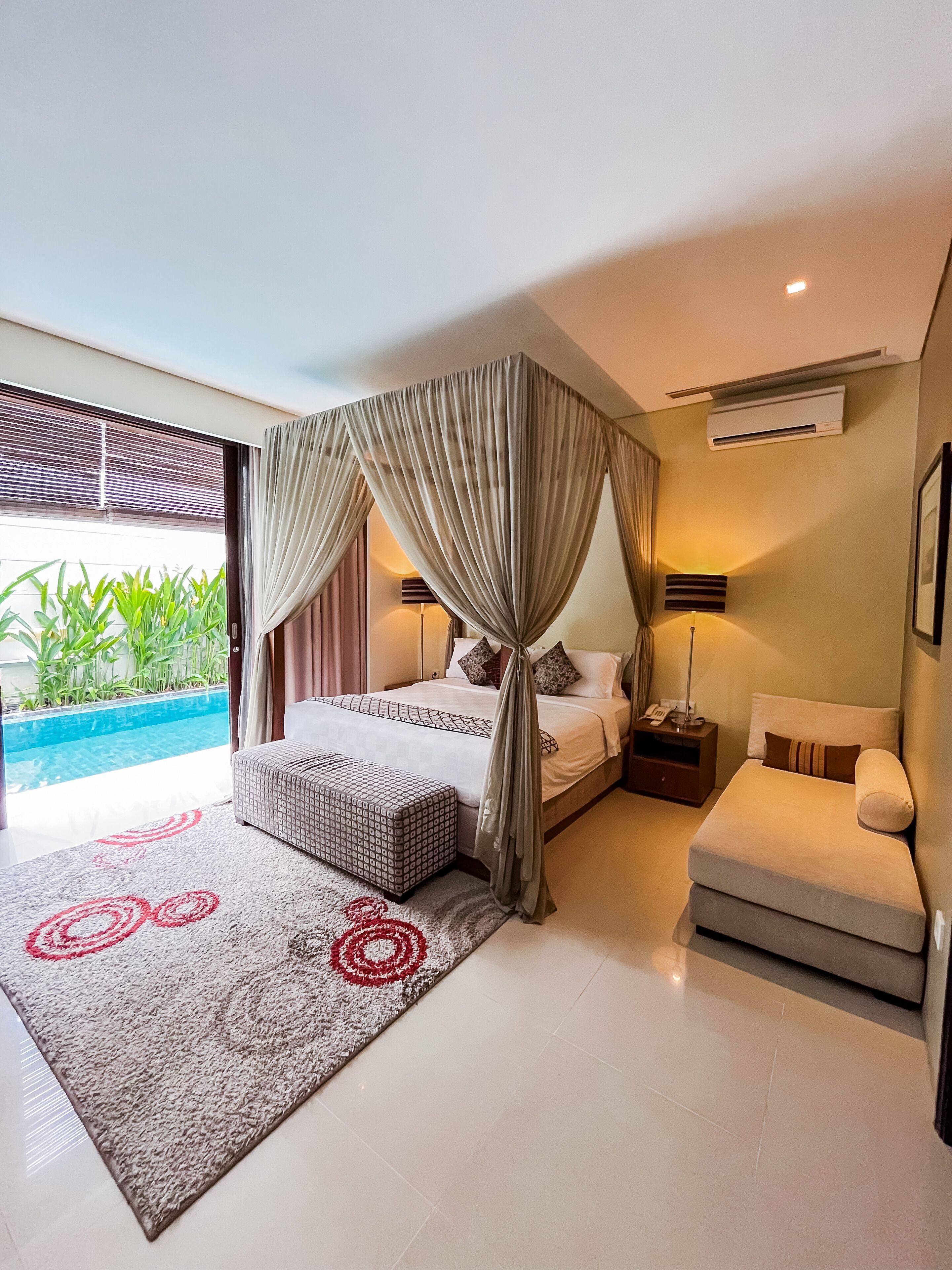 A modern bedroom with a large bed, a sitting area, and a view of a swimming pool.