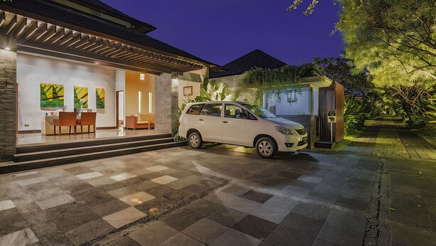 Une maison moderne avec une voiture garée devant, une entrée bien éclairée et une allée pavée.