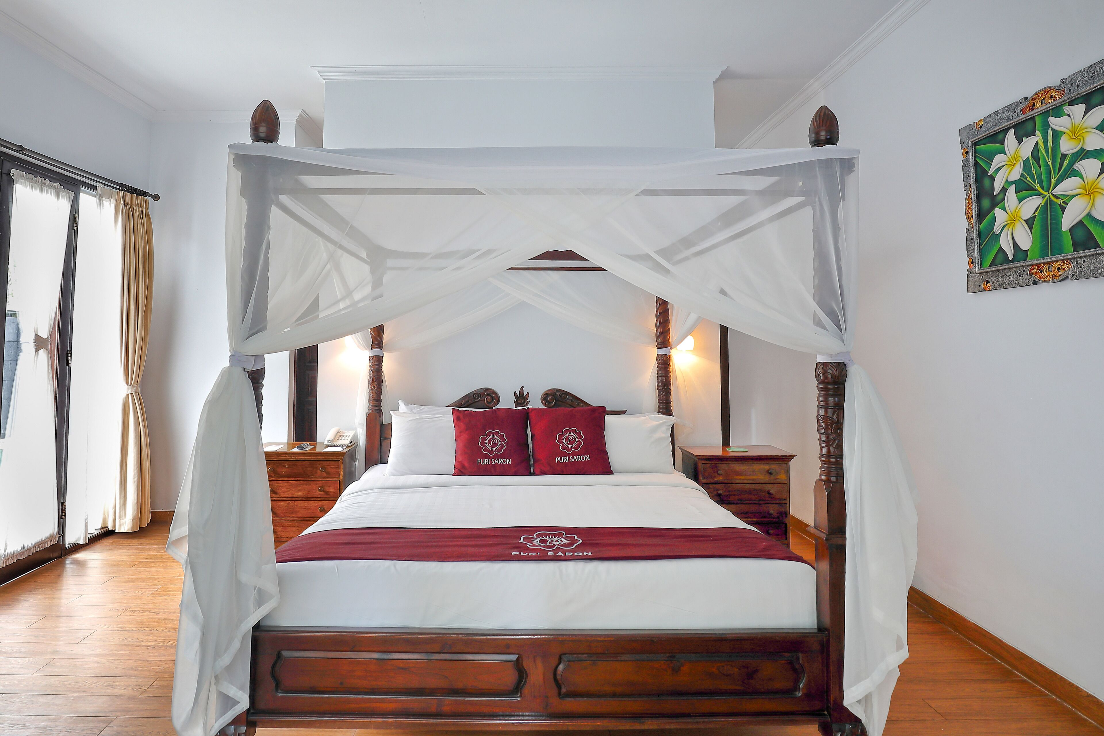 Una cama con dosel sobre cuatro pilares, con cabecera de madera, ropa de cama blanca y dos almohadones decorativos.