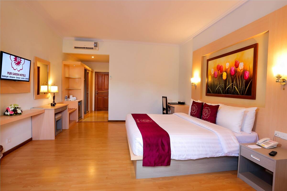 A hotel room with a bed, bedside table, lamp, and a painting of tulips.