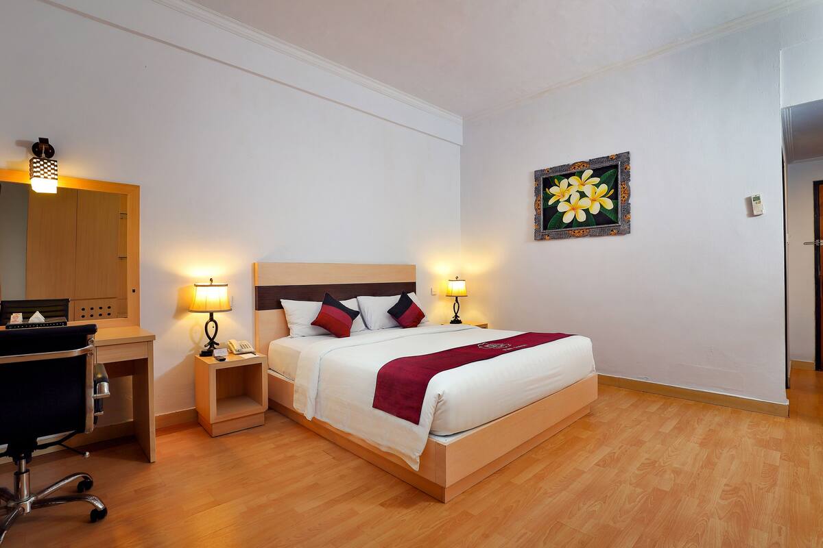 A neatly arranged hotel room with a bed, bedside lamps, a desk with a chair, and a wall-mounted artwork.