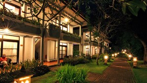 A hotel with a pathway leading to the entrance, surrounded by greenery and illuminated by outdoor lights. - Puri Saron Seminyak (Seminyak)