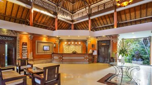 A spacious lobby with a high ceiling, a reception desk, seating area, and a view of the outdoors. - Puri Saron Seminyak (Seminyak)