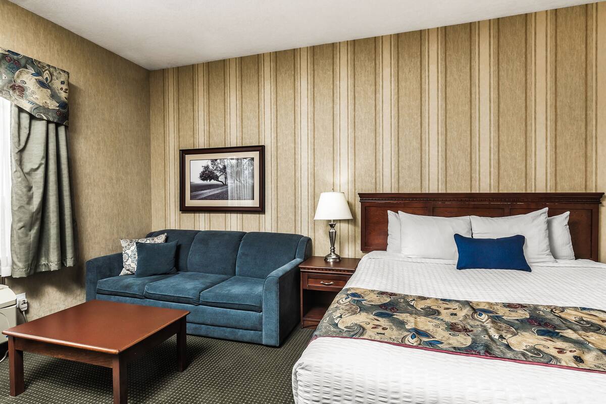 A hotel room with a bed, a blue sofa, a wooden table, and a nightstand with a lamp.