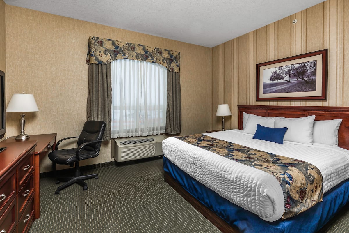 A hotel room with a large bed, a desk with a chair, a window with curtains, and a framed picture on the wall.