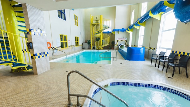 An indoor swimming pool with a slide, a hot tub, and a seating area with chairs. - Redwood Inn & Suites - Grande Prairie (Clairmont)