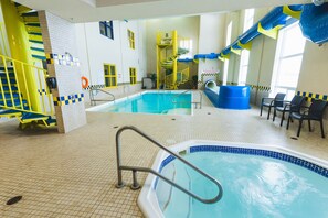 Una piscina interior con tobogán, una bañera de hidromasaje y una zona de estar con sillones.