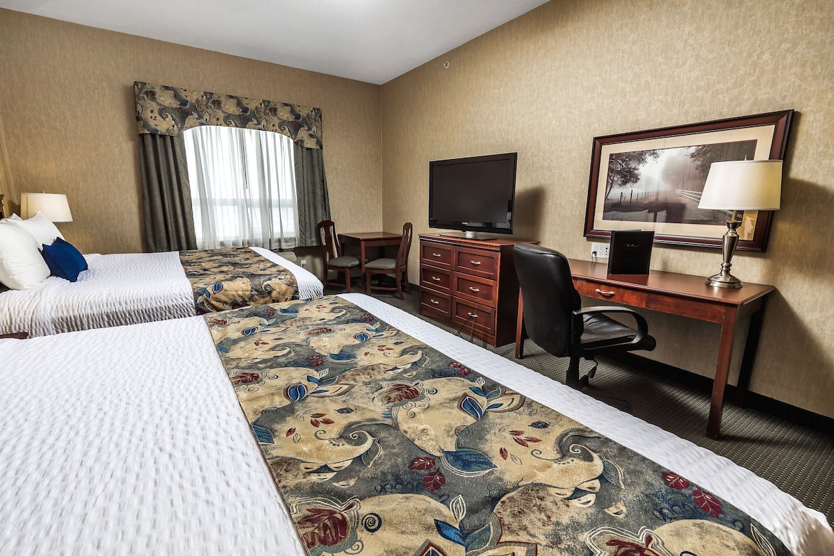 A hotel room with two beds, a desk with a television, a chair, and a desk lamp.