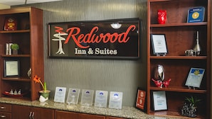 A reception desk at Redwood Inn & Suites with a large sign, framed awards, and a plant. - Redwood Inn & Suites - Grande Prairie (Clairmont)