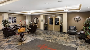 A lobby with a leather sofa, a coffee table, a reception desk, and a reception area with a desk and chairs. - Redwood Inn & Suites - Grande Prairie (Clairmont)