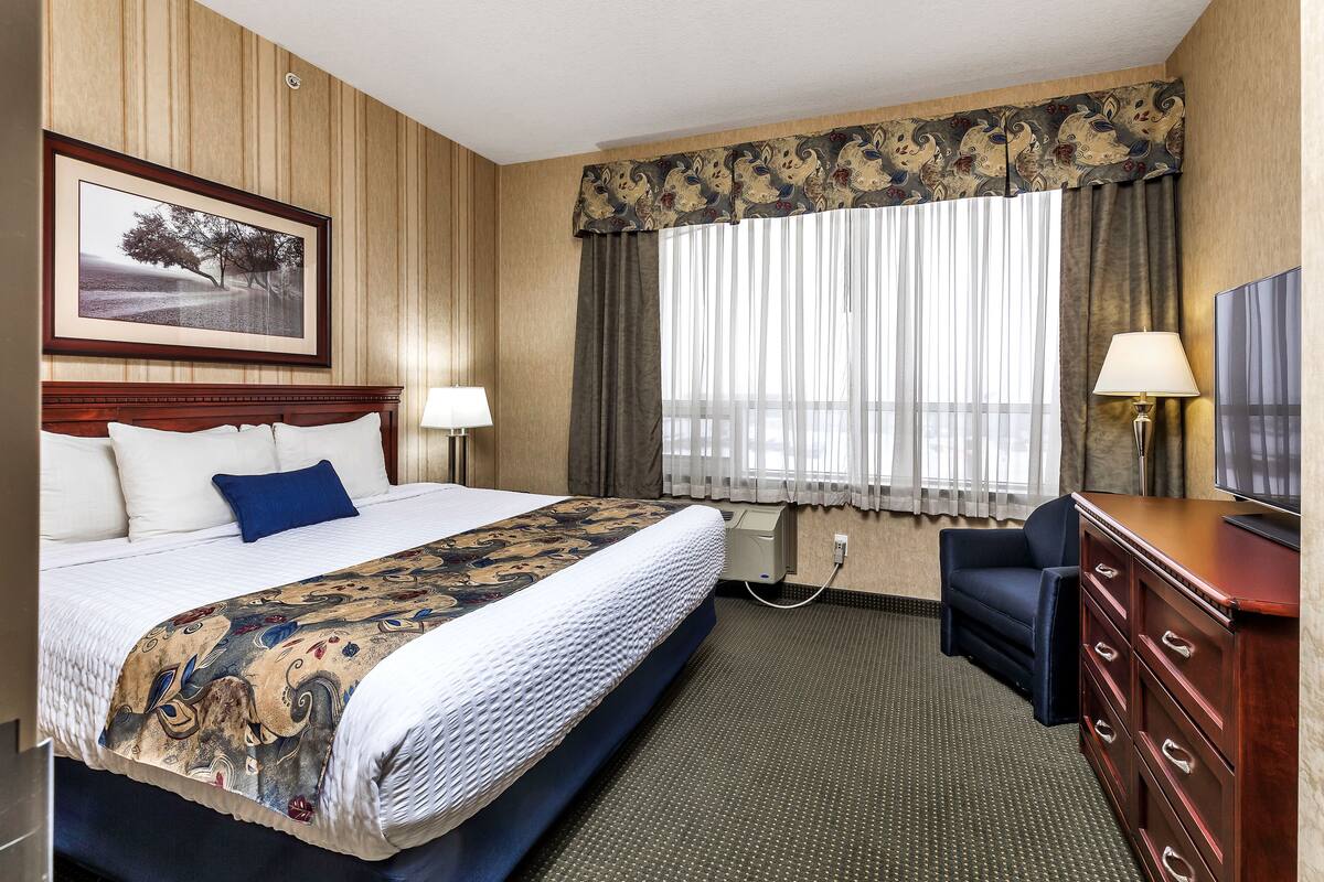 A hotel room with a large bed, a desk, a chair, a television, and a window with curtains.