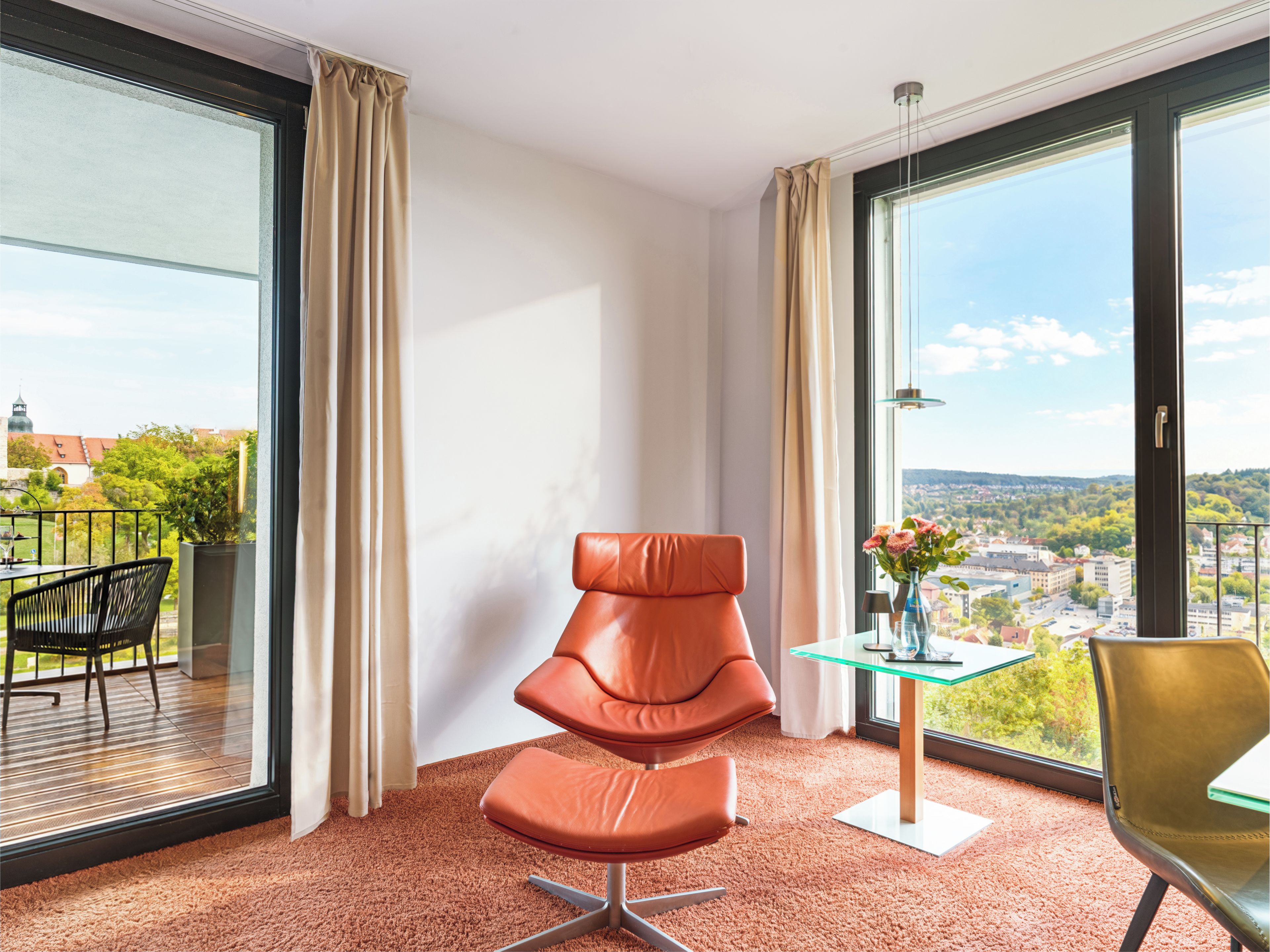 A modern room with a large window, a chair, a small table, and a view of a cityscape.