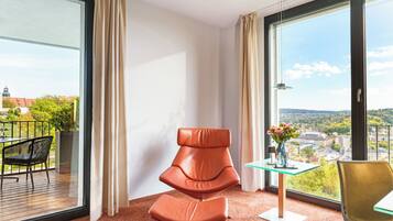 Una habitación moderna con un ventanal grande, una silla, una mesita y vistas a un paisaje urbano.