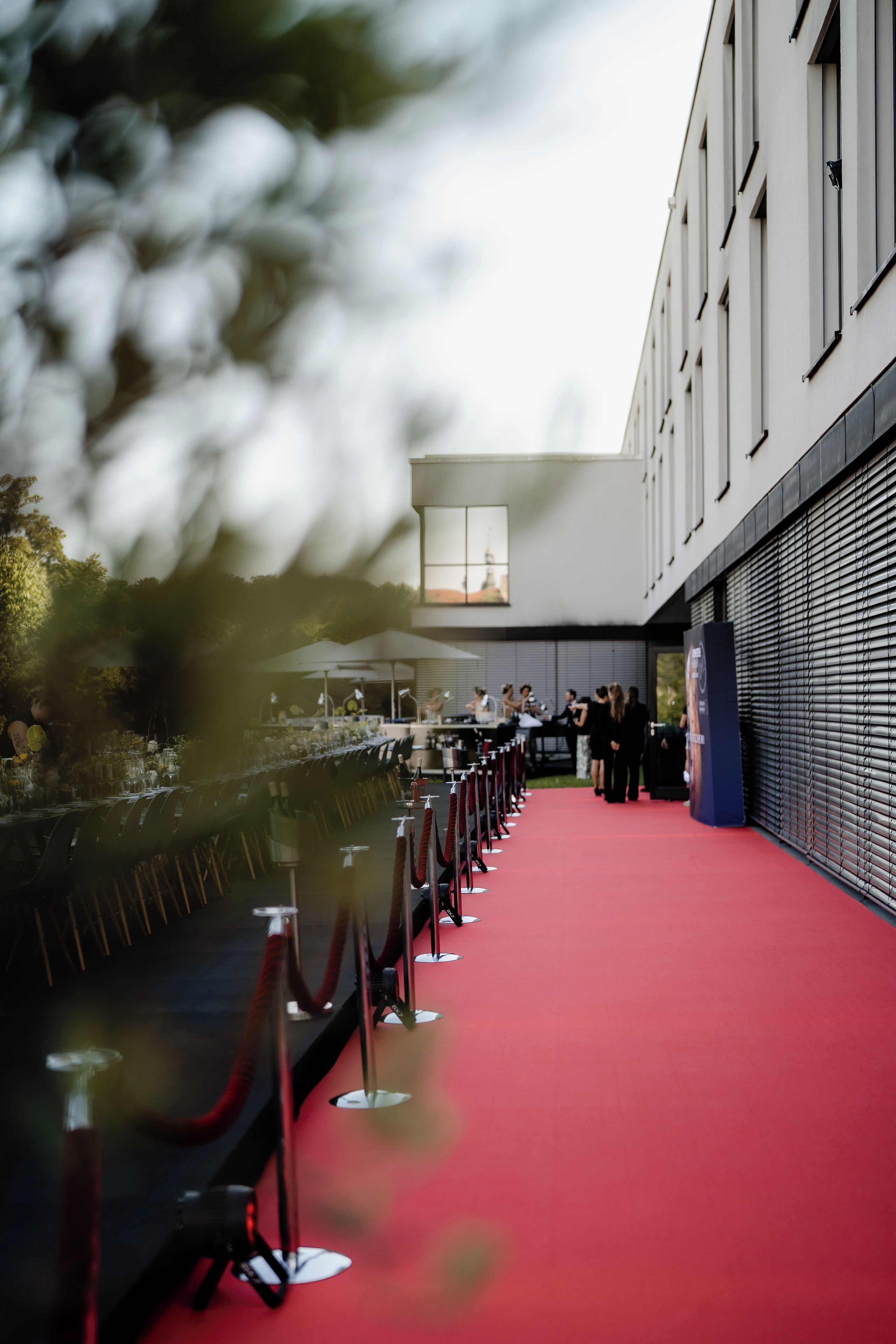 Ein Event mit rotem Teppich, ein langer Tisch für Gäste gedeckt, ein roter Teppich und ein Gebäude mit großen Fenstern im Hintergrund.