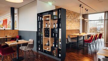 Un interior de restaurante moderno con mesas de madera, sillas rojas y grises, una exhibición de vinos y una pared de ladrillo.