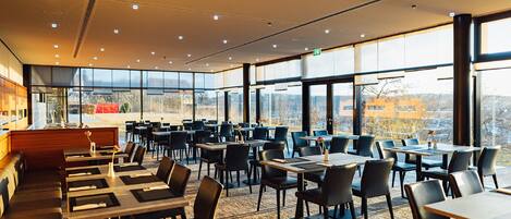 A spacious restaurant with high ceilings, large windows, and a view of the cityscape.