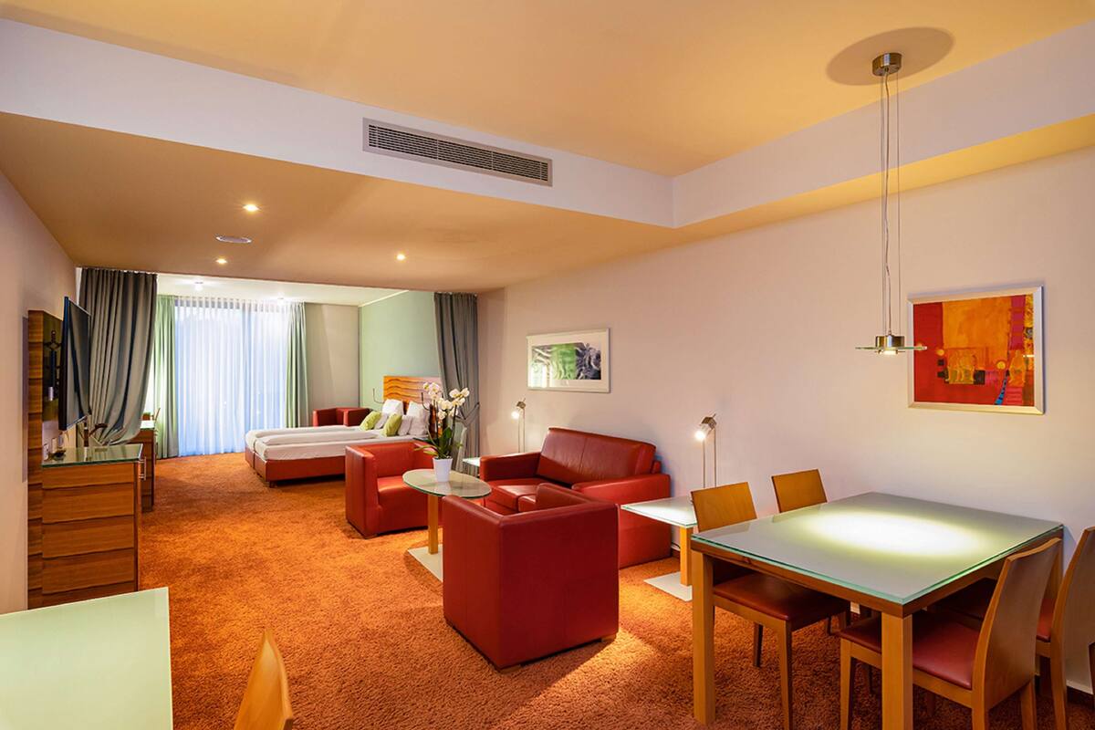 A hotel room with a living area, a dining table, and a separate bedroom with a bed.