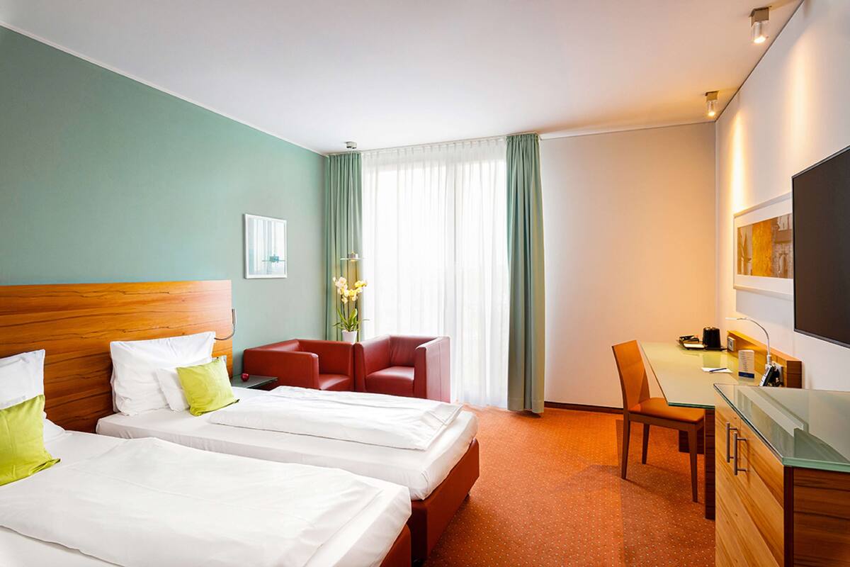 A hotel room with two beds, a desk, a chair, and a television.