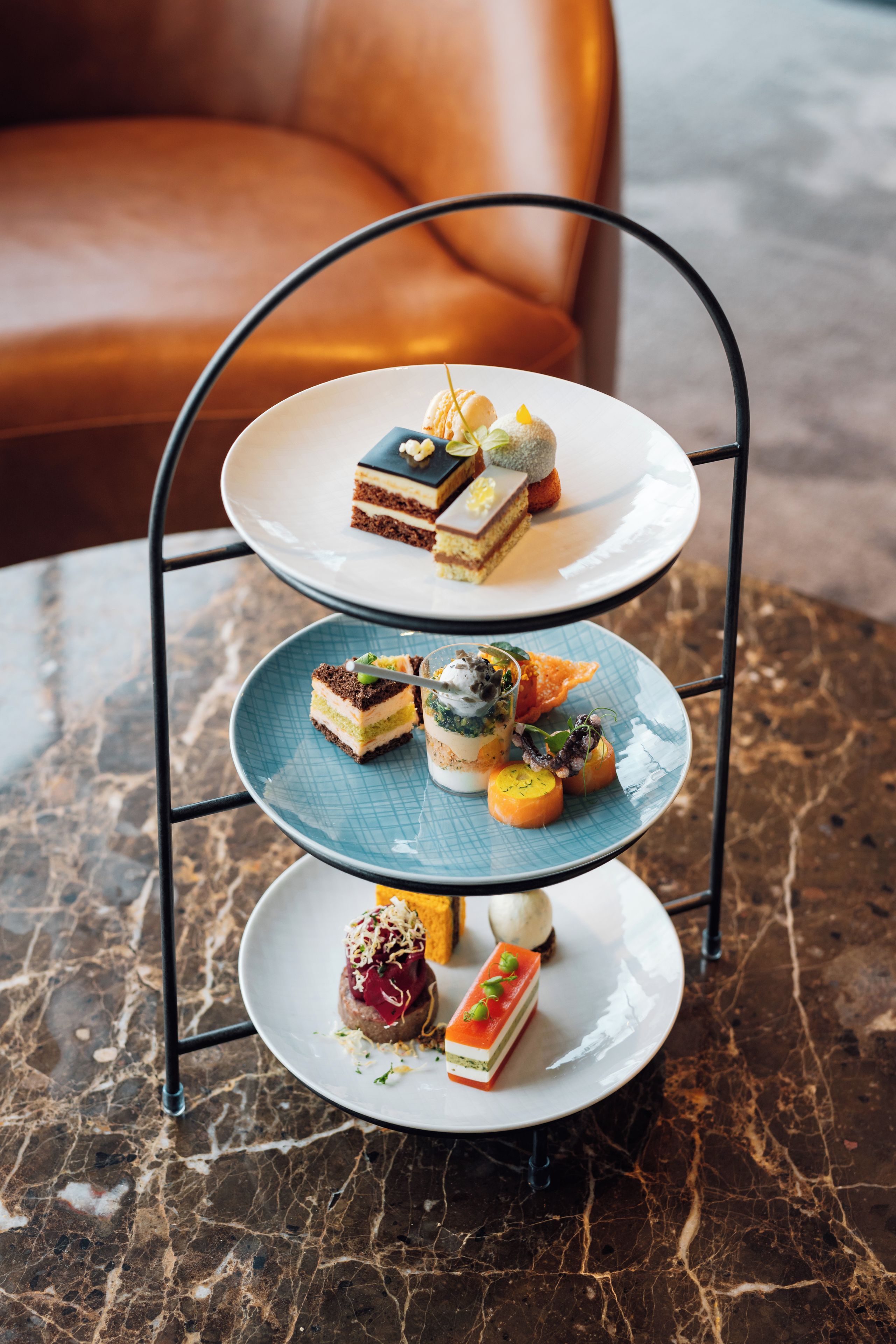 A three-tiered dessert stand with various pastries and desserts on a marble table.