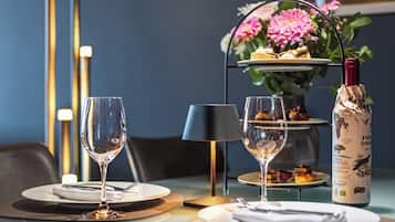 A dining table set with plates, cutlery, and wine glasses, with a bottle of wine and a vase of flowers in the background.