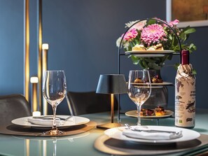 Ein Esstisch ist gedeckt mit Tellern, Besteck und Weingläsern, im Hintergrund steht eine Weinflasche und eine Blumenvase.