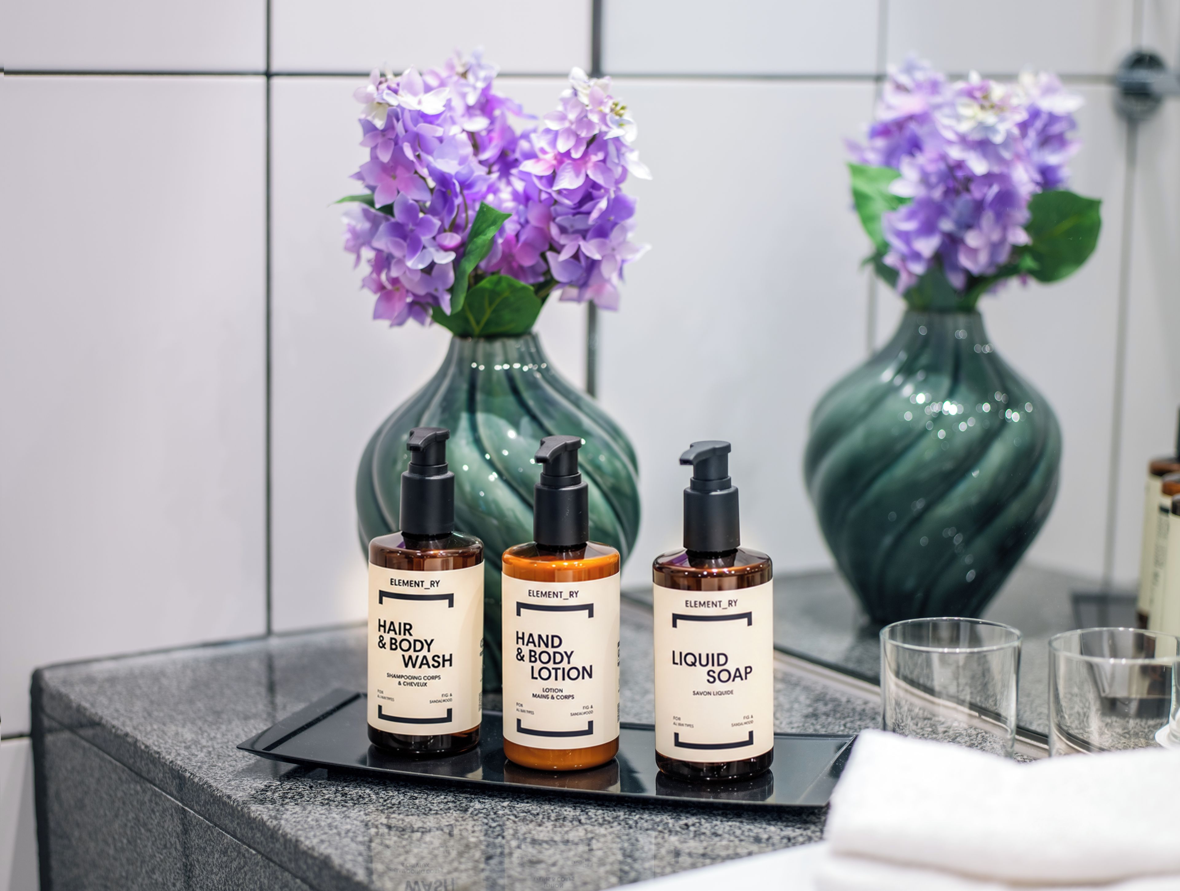 Un mobile bagno con tre prodotti Element_Ry: detergente per capelli e corpo, lozione per mani e corpo e sapone liquido.