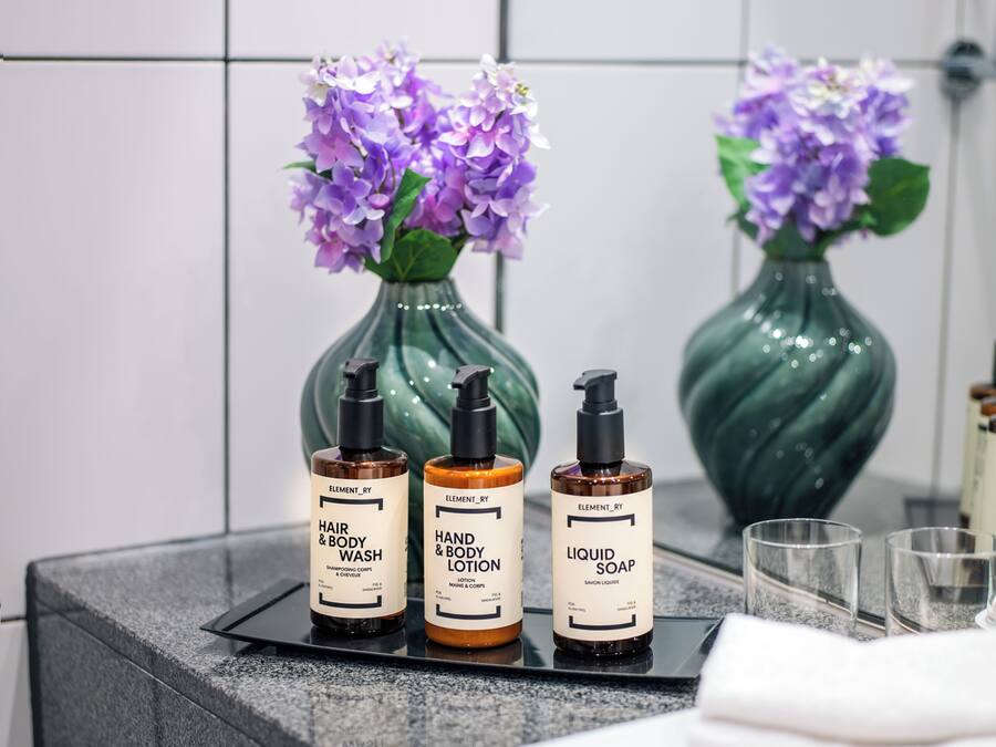 Un meuble-lavabo pour la salle de bain comprenant trois produits de la gamme Element_Ry : un gel lavant pour les cheveux et le corps, une lotion pour les mains et le corps, et un savon liquide.
