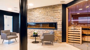 Un vestíbulo moderno con una pared de piedra, una chimenea, dos sillones grises y una mesita con una planta.