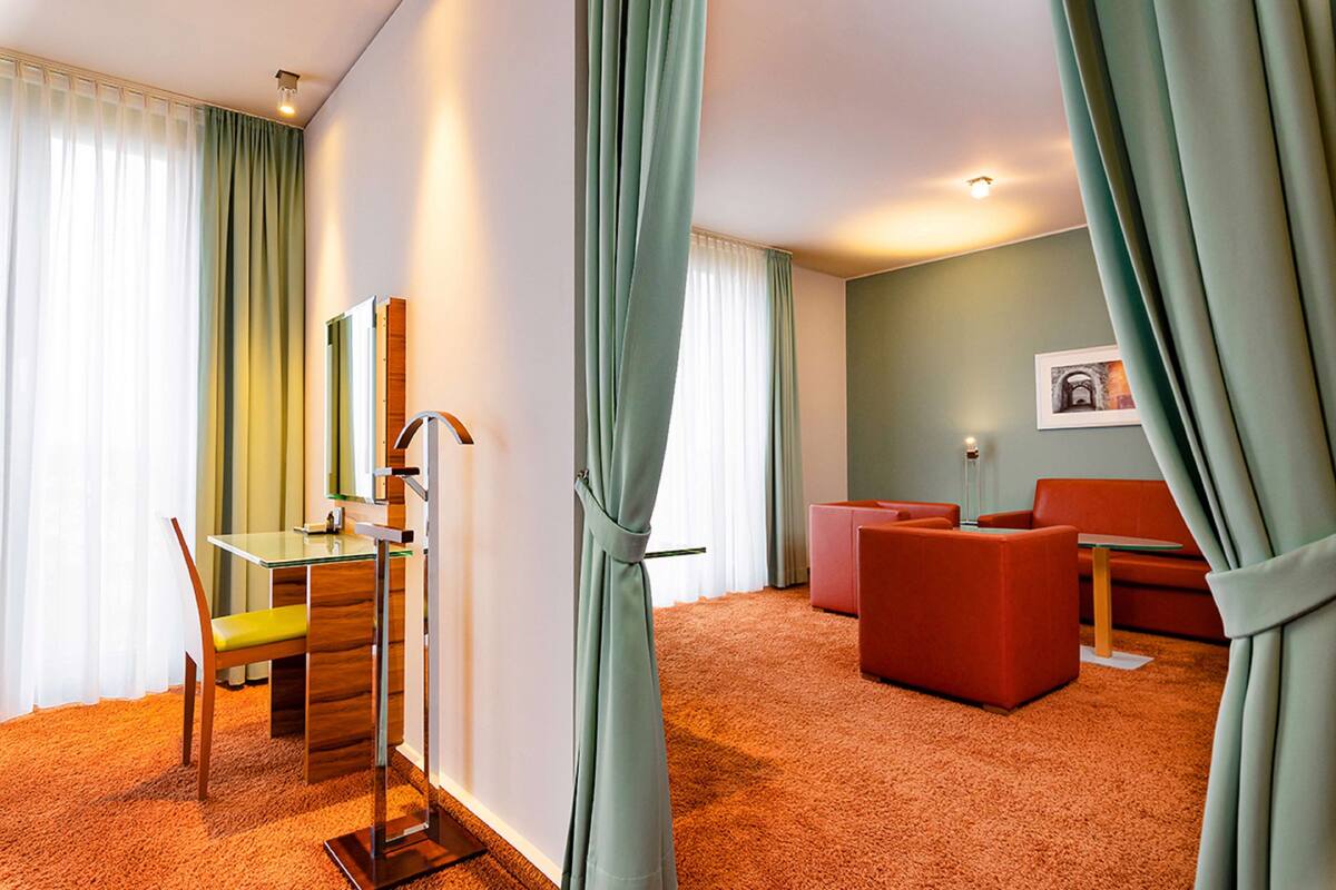 A hotel room with a desk, chair, and a sofa.