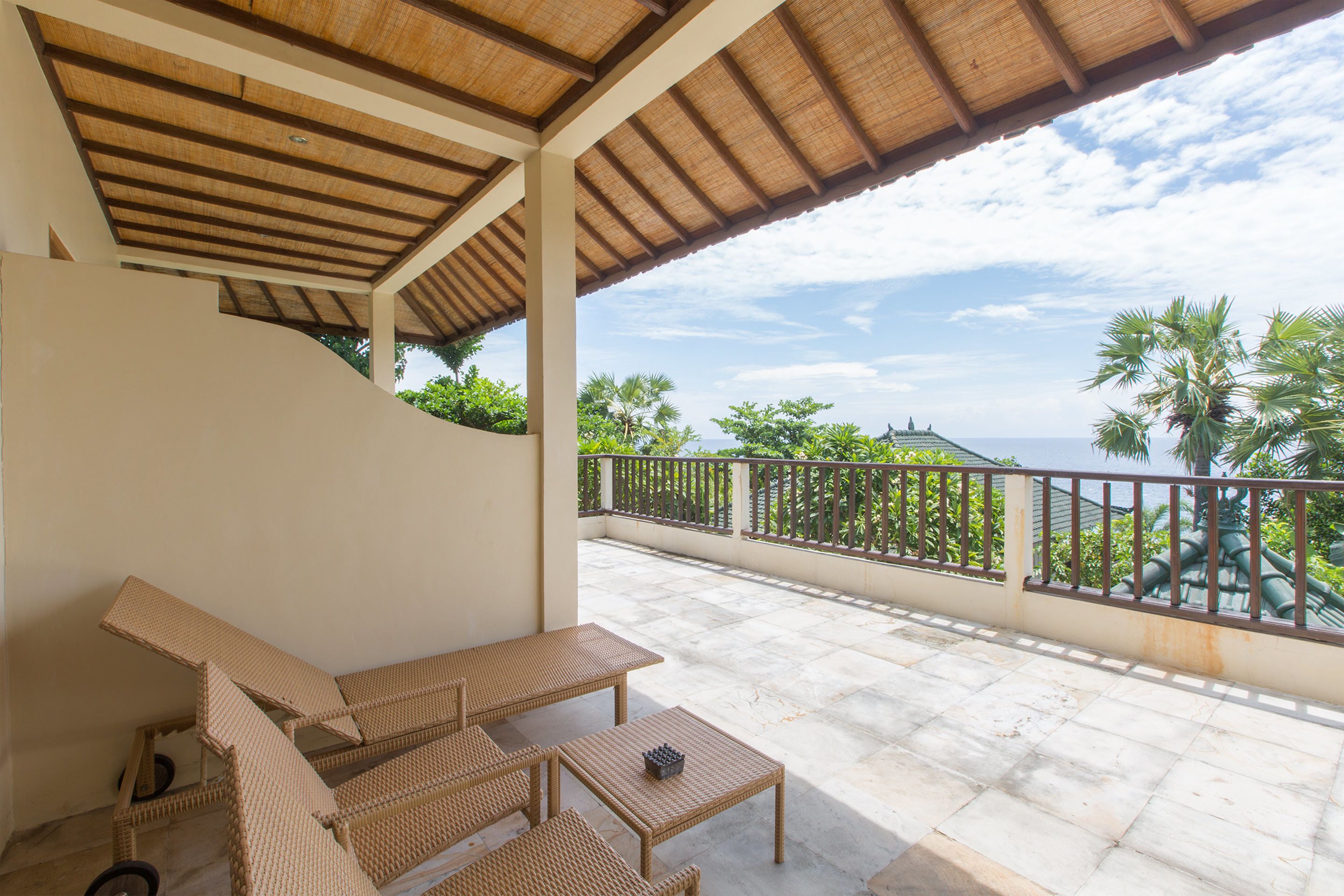 A covered outdoor seating area with wicker furniture and a view of palm trees and mountains.