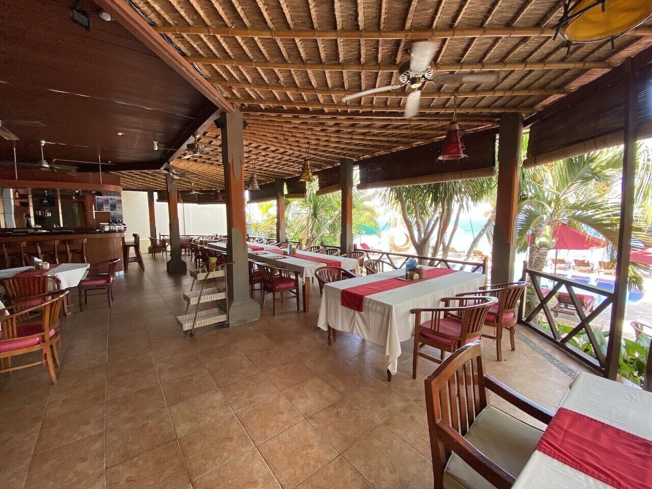 Ein überdachter Essbereich im Freien mit Tischen, Stühlen und einer Bar, mit Blick auf das Meer.