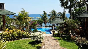 Zona de piscina con vista al océano, rodeada de plantas tropicales y un sendero de piedra.