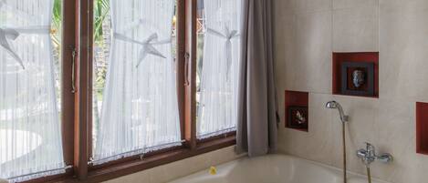 A bathroom with a large bathtub, a window with curtains, and a shower area.