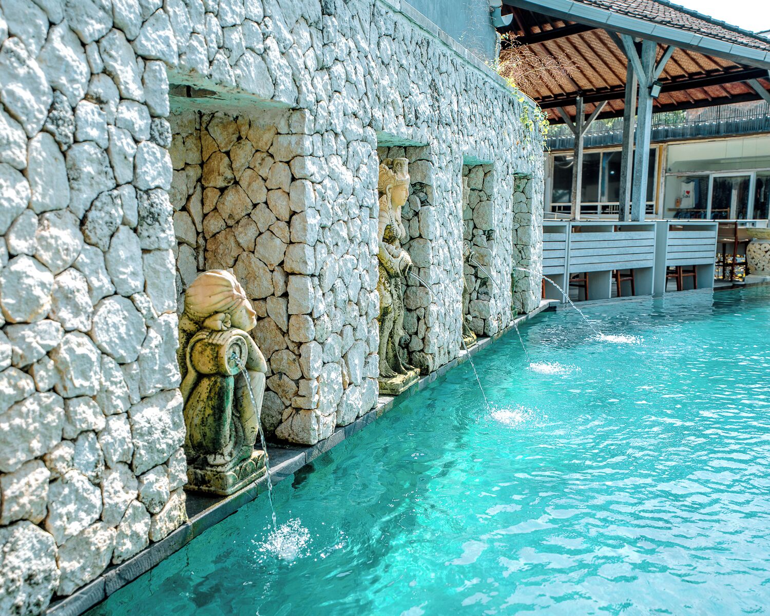 A stone building with a pool, a statue, and a covered area with a tiled roof.