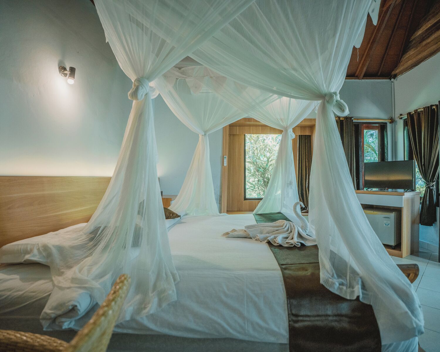 Ein Zimmer mit Himmelsbett, Fernseher und einem Fenster mit Blick auf Grünflächen.