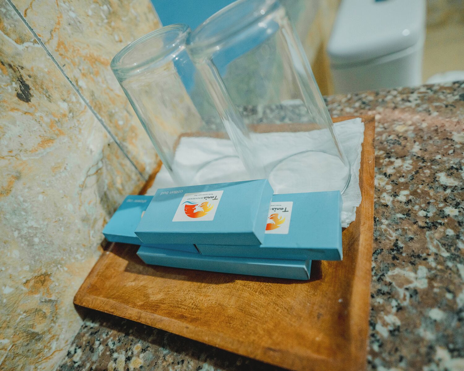 A wooden tray with two blue boxes and two clear glass containers on a granite countertop.