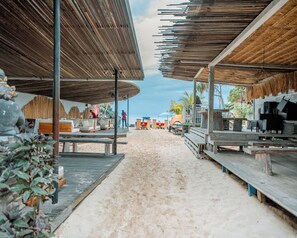 A beachside restaurant with outdoor seating, a thatched roof, and a view of the ocean.