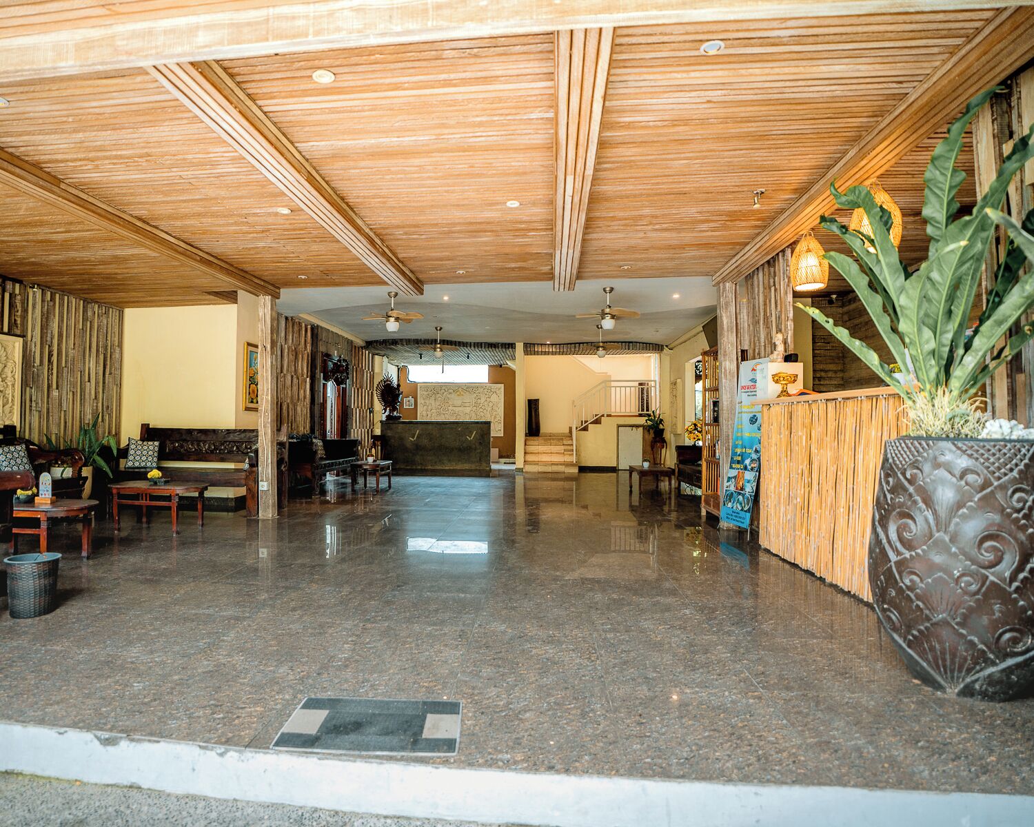 A spacious lobby with a wooden ceiling, a reception desk, seating area, and a large potted plant.