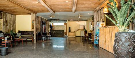 A spacious lobby with a wooden ceiling, a reception desk, seating area, and a large potted plant.