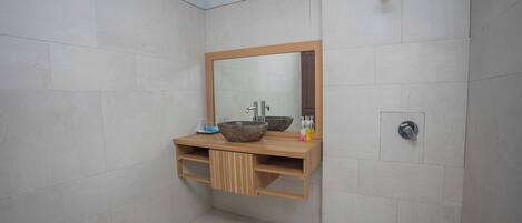 A bathroom with a wooden vanity, a large mirror, a vessel sink, and a shower area.